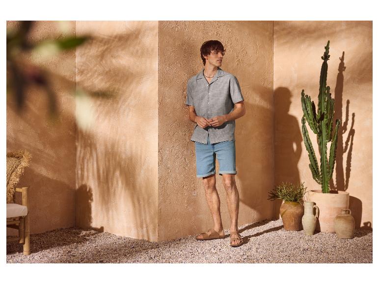Homme en chemise à manches courtes et short en jean, sandales, dans un décor méditerranéen.