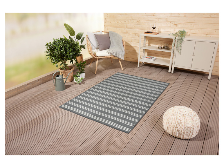 Un tapis d'extérieur rayé sur une terrasse en bois avec une chaise et un pouf.
