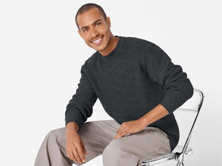 Un homme portant un pull gris foncé et un pantalon beige assis sur une chaise.