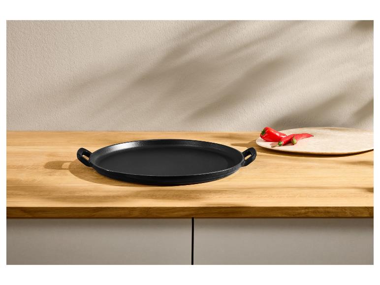 Poêle ronde en fonte noire sur une table en bois avec des poivrons rouges.