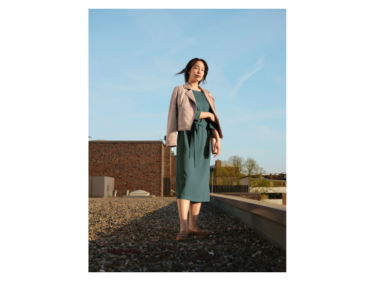Une femme en robe verte et en veste en cuir rose sur un toit.