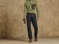 Un homme porte un pantalon noir, un pull vert et tient des jumelles.