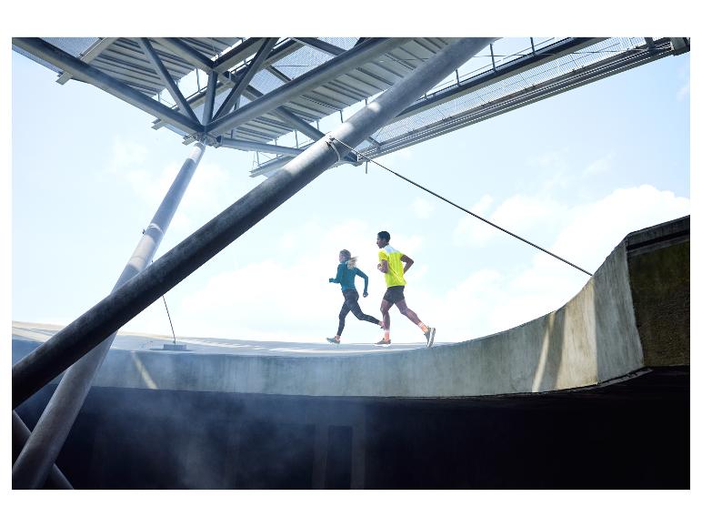 Deux coureurs s'entraînent sur une piste incurvée, sous une structure métallique.