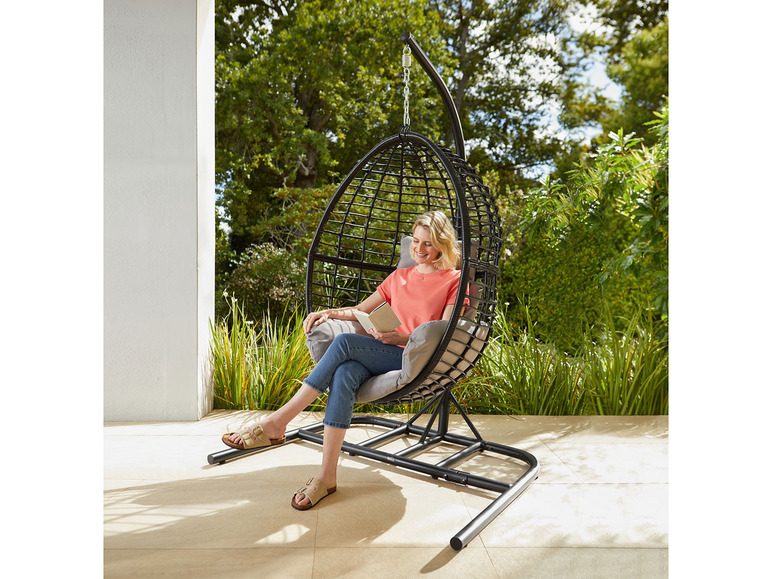 Une femme lit dans un fauteuil suspendu dans le jardin.