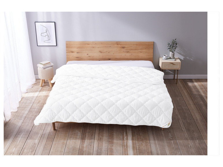 Une couette blanche avec un motif en losanges piqués sur un lit en bois.