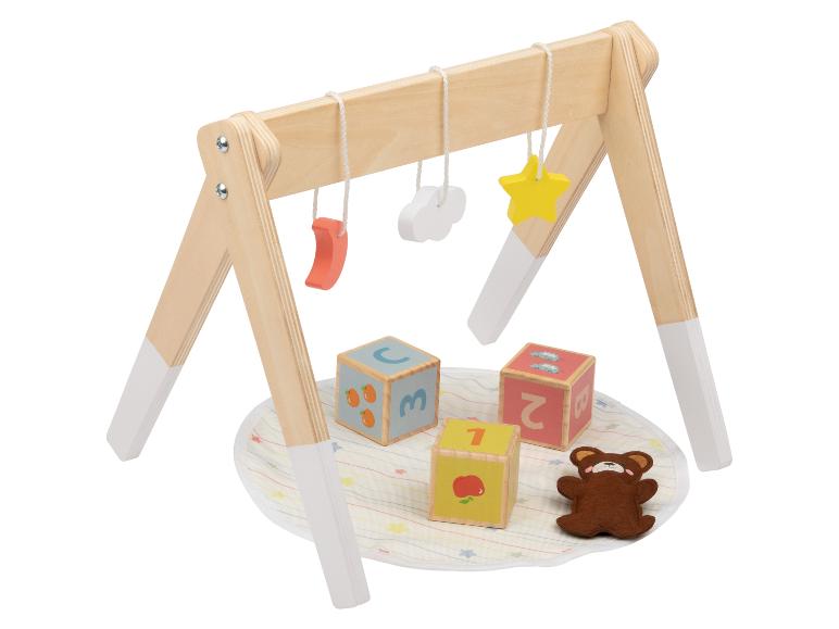 Portique d'activités en bois avec jouets suspendus, blocs et un ours en peluche.