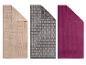 Trois serviettes de bain : beige à motifs géométriques, grise à motifs de briques et violette unie.
