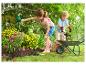 Enfants jardinant avec une brouette en jouet et des outils dans un parterre de fleurs.