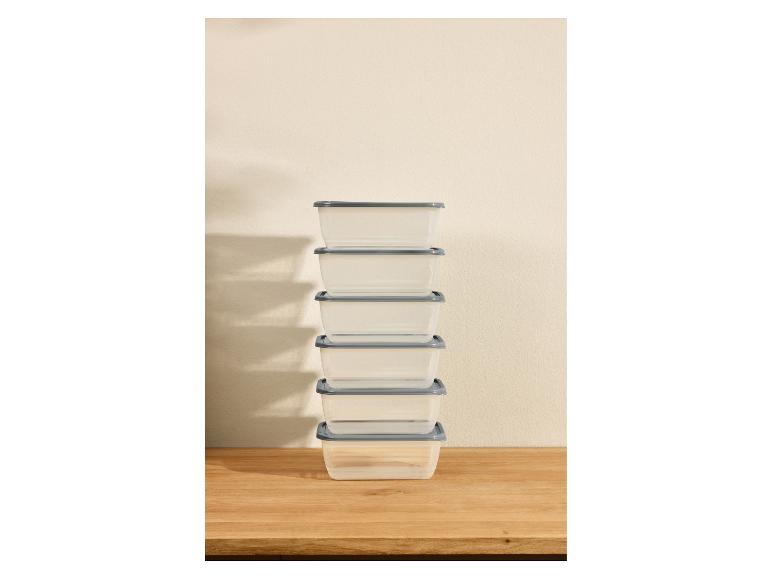 Pile de récipients alimentaires transparents avec couvercles gris sur un comptoir en bois.