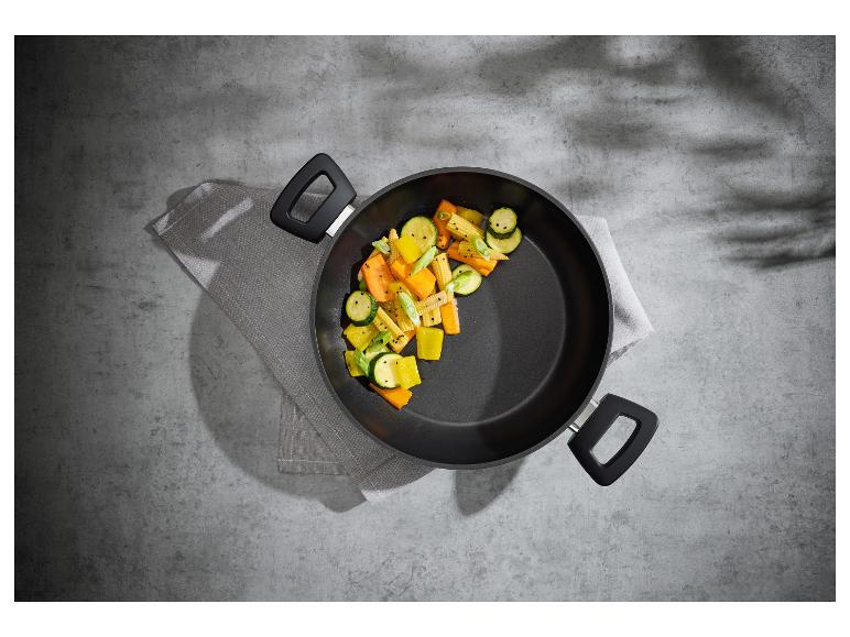 Wok avec légumes sautés (courgettes, carottes, épis de maïs) sur fond gris.