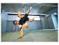 Homme en veste de sport et short dans une pose acrobatique dans un hall.