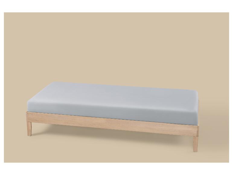 Matelas gris clair sur un cadre de lit en bois sur fond beige.