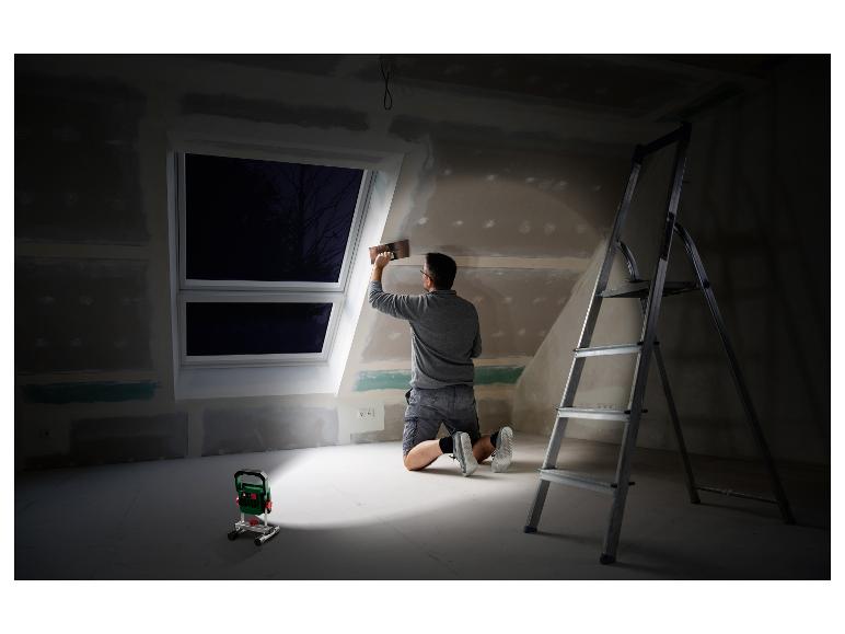 Un homme installe un mur dans une pièce inachevée avec une lampe de travail Bosch.