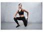 Femme en soutien-gorge de sport noir, leggings et baskets s'étirant devant un fond gris.