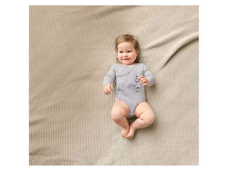 Un bébé allongé sur une couverture beige, portant un body gris avec un ours imprimé.