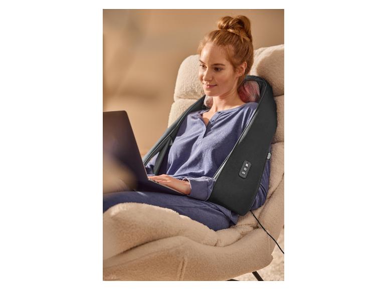 Femme détendue dans un fauteuil utilisant un masseur de cou et d'épaules tout en travaillant sur un ordinateur portable.