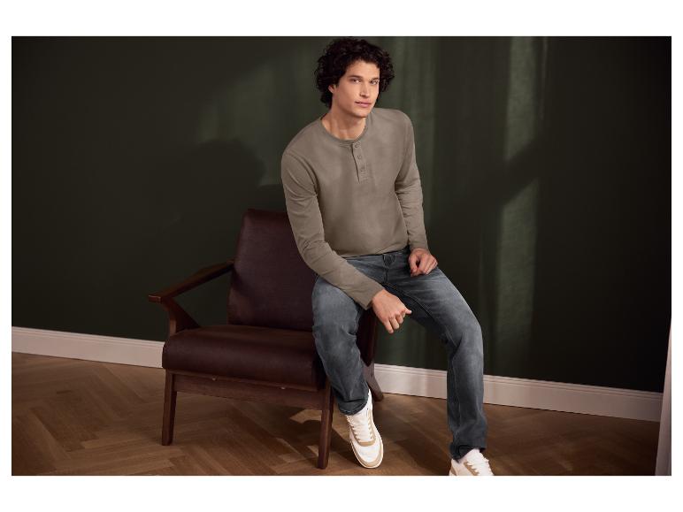 Homme en t-shirt marron à manches longues et jean bleu, assis dans un fauteuil en cuir.