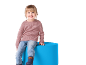 Fille souriante assise sur un pouf bleu, portant un pull rose et un jean.