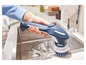Une main tient une brosse de nettoyage bleue et blanche qui nettoie un évier.