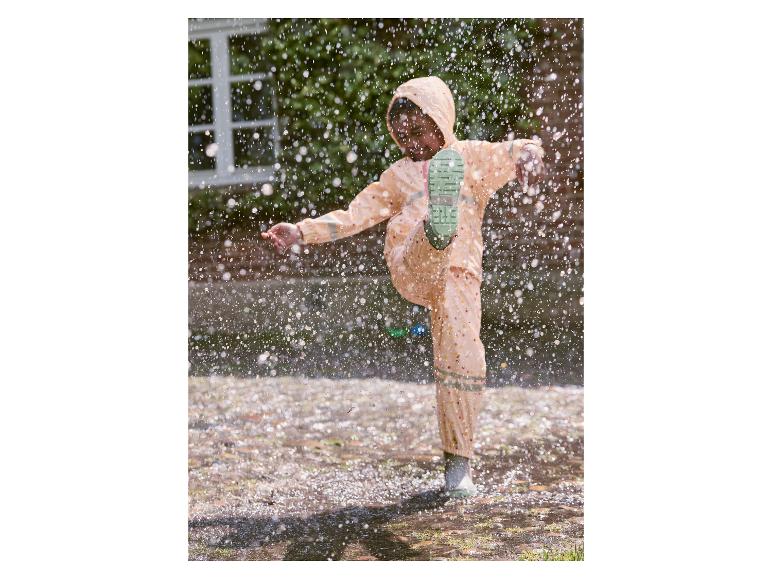 Enfant en imperméable et bottes de pluie sautant dans une flaque.