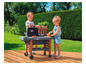 Deux enfants jouent avec un barbecue Smoby sur une terrasse en bois.