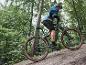 Un homme roule à vélo électrique de montagne gris avec des pneus Maxxis dans une forêt.