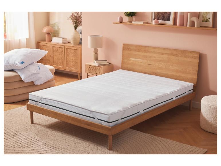 Surmatelas blanc sur un lit en bois dans une chambre aux murs roses.