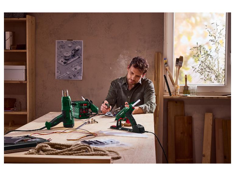 Homme utilisant un fer à souder et un pistolet à colle Parkside sur un établi.