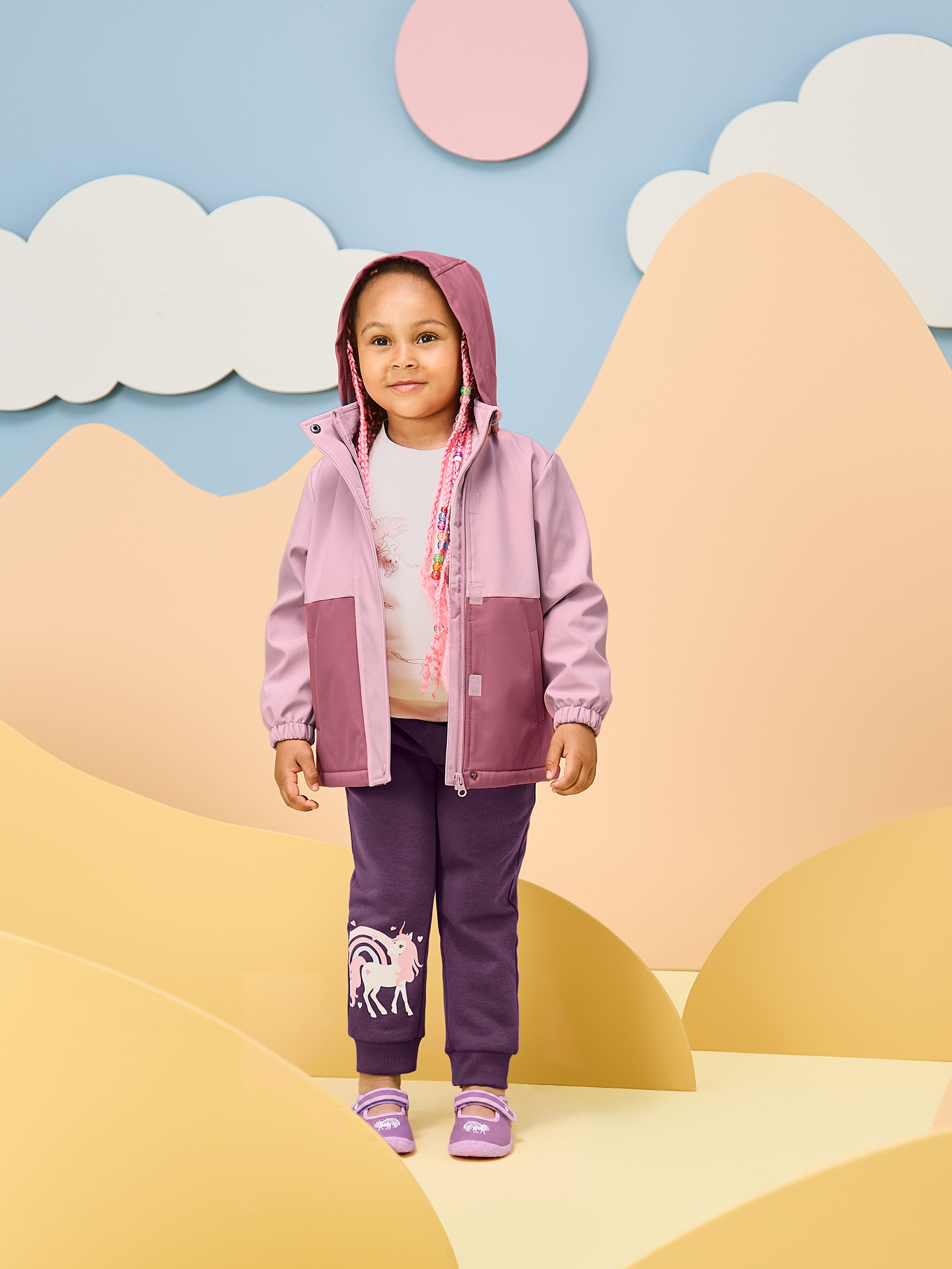 Fille en veste rose et pantalon violet avec licorne, dans un décor ludique.