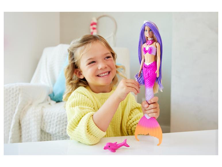 Fille souriante jouant avec une poupée sirène et un jouet dauphin rose.