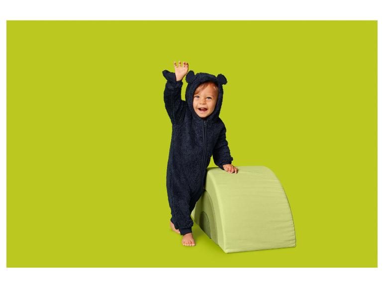 Tout-petit en costume d'ours, souriant et saluant à côté d'un jouet doux.
