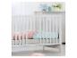 Lit de bébé blanc avec literie rose et bleue, avec des jouets en peluche.