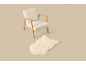 Fauteuil crème avec cadre en bois et tapis moelleux sur fond beige.