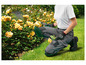 Genouillères de jardin, gants et sécateur dans un jardin avec des roses jaunes.