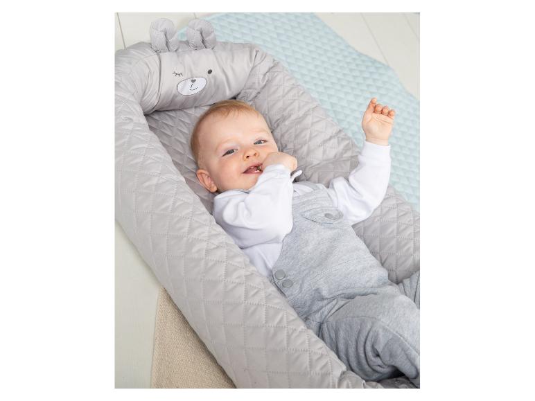 Bébé heureux dans un nid gris avec un visage et des oreilles d'ours, allongé sur un tapis bleu clair.