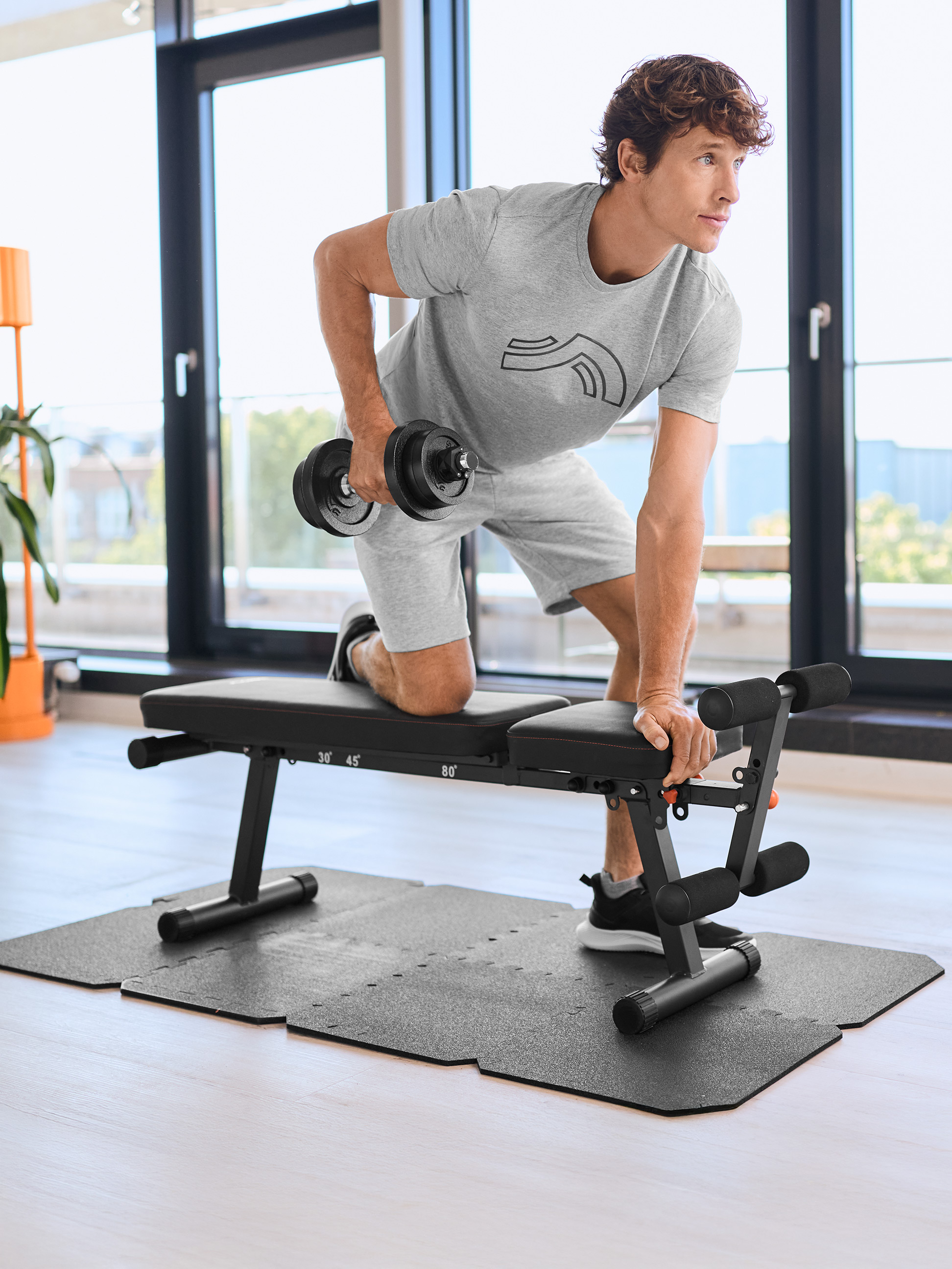 Homme s'entraînant avec un haltère et un banc de musculation sur un tapis d'exercice.