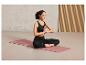 Une femme en tenue de sport assise en méditation sur un tapis de yoga rose.