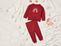 Un sweat-shirt rouge avec un arc-en-ciel et un pantalon assorti sur une couverture blanche.
