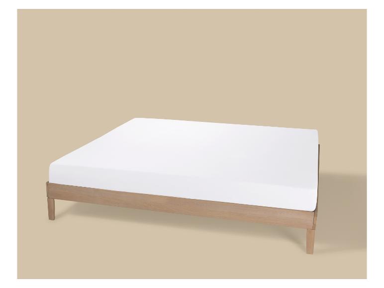 Lit en bois avec matelas blanc sur fond beige.