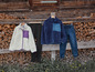 Deux vestes en polaire, un pantalon noir et un jean sont suspendus devant un hangar en bois.