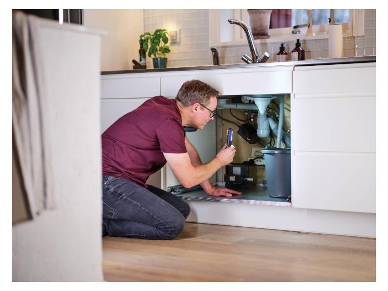 Homme avec lampe de travail LIVARNO® «The Inspector» inspectant sous l'évier.