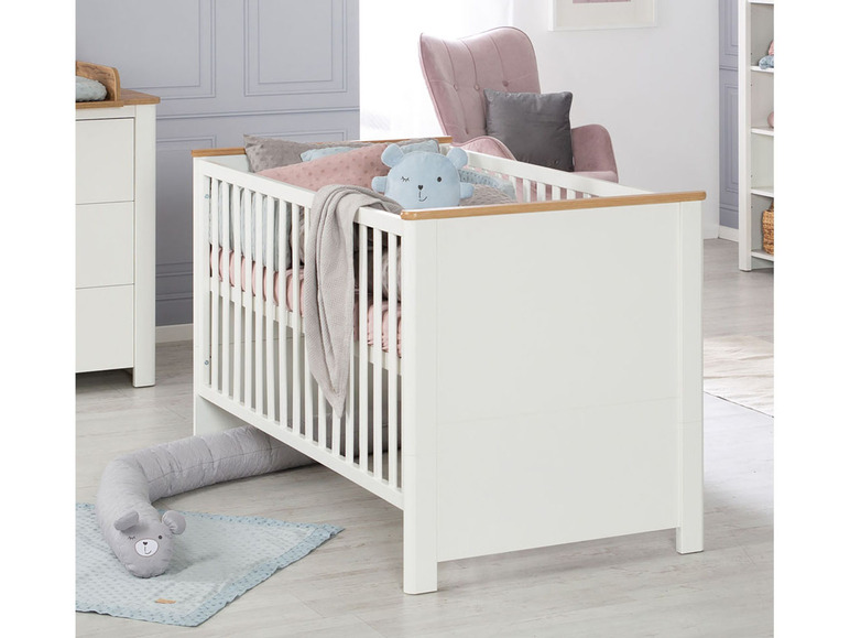 Un lit bébé blanc avec des détails en bois et un ourson en peluche gris.