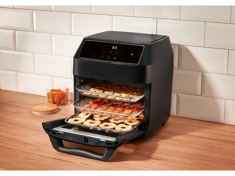 Friteuse à air noire avec fruits secs sur des grilles, sur un comptoir de cuisine en bois.