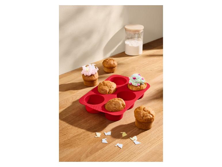 Moule à muffins en silicone rouge avec des muffins, certains décorés de glaçage.