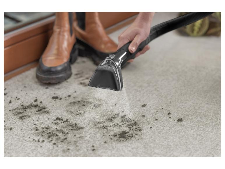 Une personne nettoie un tapis sale avec un nettoyeur de tapis, portant des bottes marron.
