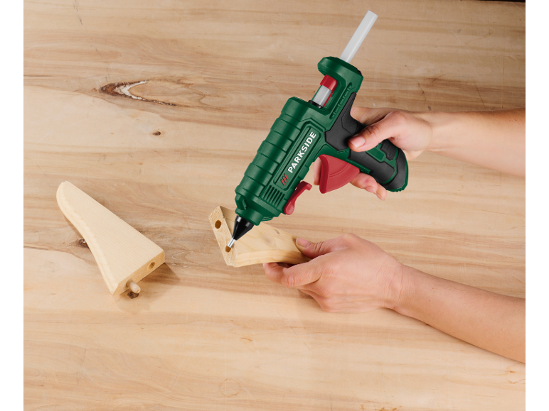 Main utilisant un pistolet à colle chaude sur des pièces en bois sur une table en bois.