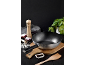 Poêle wok avec manche noir, épices et ustensiles de cuisine sur bois.