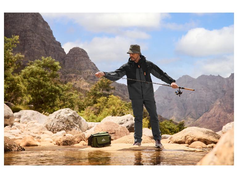 Homme en veste et pantalon de pêche, avec chapeau, pêchant dans un ruisseau de montagne.