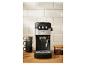 Machine à expresso noire et argentée sur un comptoir en bois avec des tasses et des grains de café.