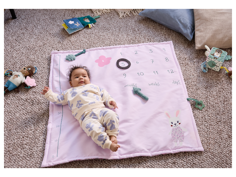 Un bébé est allongé sur un tapis rose avec des nombres et des jouets.